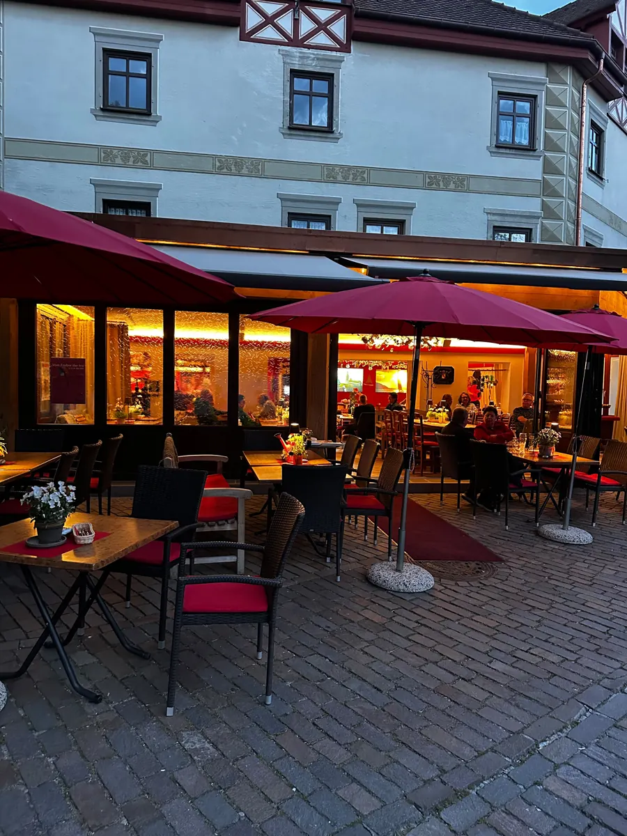 Das Weinhaus Renker am Abend: beleuchtete Stube, rote Sonnenschirme und Tische auf dem Pflaster davor