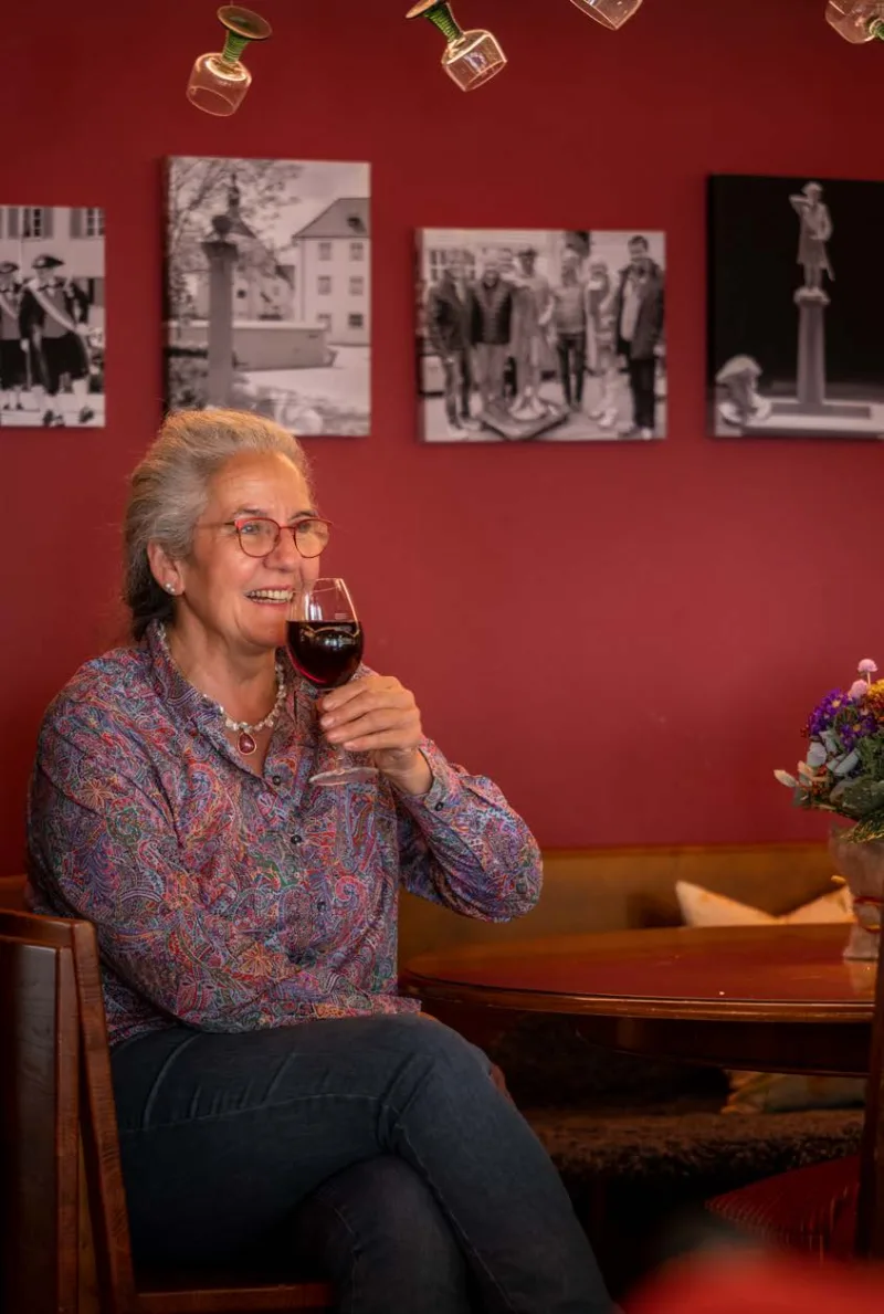 Elke Renker lachend mit einem Glas Rotwein in ihrer Weinstube